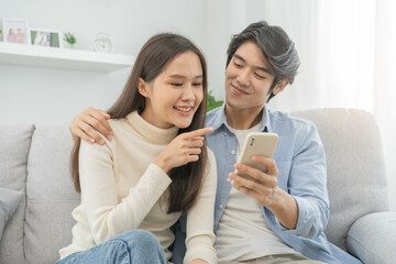 Happy couple love at home,beautiful two asian young spending good time together,bonding to each other and smiling romantic on sofa in living room while man embrace woman using smartphone, mobile phone