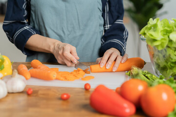 Asian young woman, girl or housewife using knife, cutting carrots on  board, on wooden table in kitchen home, preparing ingredient, recipe fresh vegetables for cooking meal. Healthy food people.