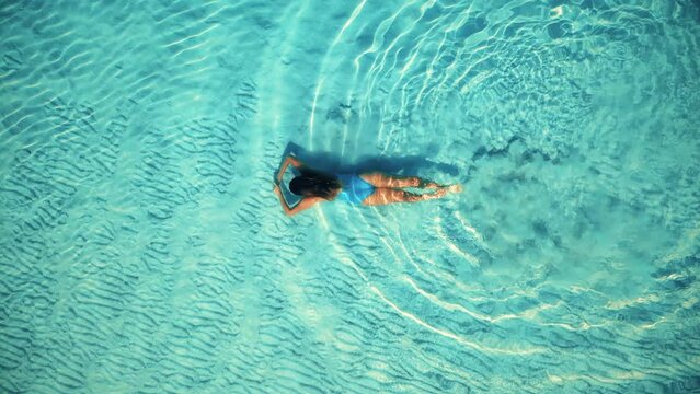 Aerial slow-motion video of young woman swims at the crystal ocean water. 