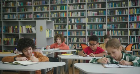 Asian teacher walks about library room watching schoolkids