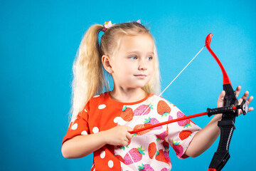 A determined girl in a red dress shoots a bow. The concept of children's games, striving for a...