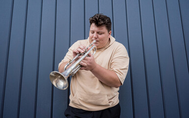Young street musician playing the trumpet near the big blue wall