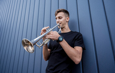 Young street musician playing the trumpet near the big blue wall © romaset