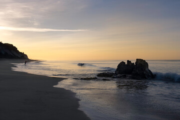 Fisherman silhouette on the ocean beach in Faro, Portugal by sunrise