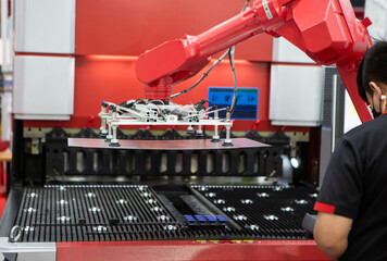 Robot arm loading metal sheet to laser cutting machine in production line. Industrial metalworking...