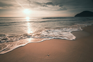 long exposure shot soft wave of the sea on the sandy beach at morning sunlight .