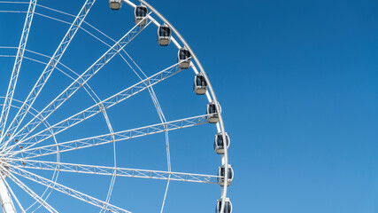 Close-up details of ferris wheel on clear blue sky background, with metal beam guides and passenger booths. Marina Mall ferris wheel, Abu Dhabi, United Arab Emirates