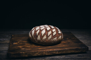 Loaf black rye bread sprinkled with flour on rustic wooden dark background.
