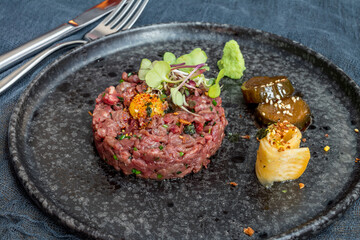 Tartare from beef with egg on black plate side view