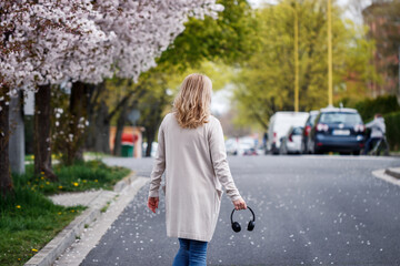 Woman with headphones walking on city street under blooming cherry trees. City life at springtime