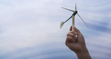 Hand holding a sustainable green energy wind turbine. The wind is moving through