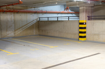Underground car park. Empty garage, parking lot with yellow black markings on the pillars. Numbered parking spaces.