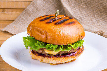 Burger with meat patty, vegetables and salad with cheese on wooden table