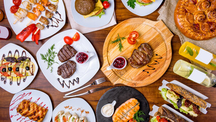 assorted dishes on table,medallions of beef,beef steak,salmon steak,caprese salad,skewers of salmon,cherry pie,lemonades,burger on wooden table top view