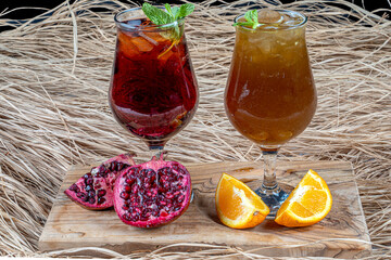Colorful icetea drink with fresh sweet fruits mint leaves in glass on the rocks on a wooden table.