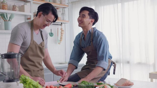 Asian gay couple tease each other very happy and romantic in their home kitchen while cooking together.