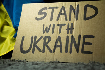 Ukrainian flag and "Stand With Ukraine" placard sign in protest manifestation against Russia invasion and war on Ukraine. Russian attack, anti-war demonstration.