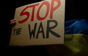 Woman holding Ukrainian flag and "Stop the War" placard sign in protest manifestation against Russia invasion on Ukraine. Russian attack, anti-war demonstration.