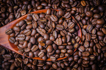 Black coffee beans in a wooden spoon.