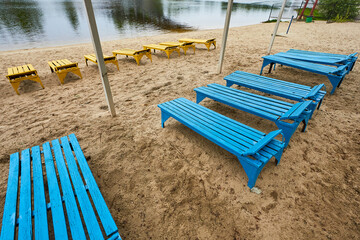 Part of the city beach. Old dirty sunbeds on the background of the city river. A place of rest in a...