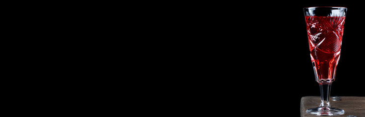 Web banner with berry liquor in crystal vintage shot glass on the wooden table against the black background. Mockup with copy space