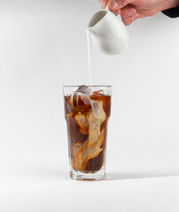 Milk is poured into cold coffee. On a light background.