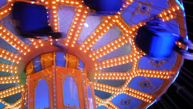 Night carousel on which visitors ride. Amusement park in the evening in colorful lights. Illuminated merry go round carousel