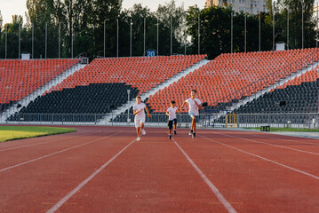 Obraz premium A large group of boys ' children are taught by a coach at the start before running at the stadium during sunset. A healthy lifestyle.