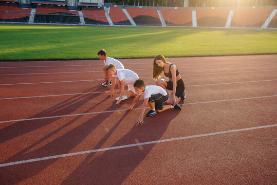 A group of boys ' children are taught by a coach at the start before running at the stadium during sunset. A healthy lifestyle.