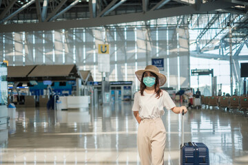 Fototapeta na wymiar Young female wearing face mask with luggage walking in airport, protection Coronavirus disease infection, Asian woman traveler with hat. Time to travel after vaccine booster dose concept
