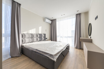 Wide corner of the bedroom in a modern style with a large bed, window, air conditioning and a round mirror