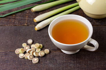 Cup of hot lemongrass tea with sliced and green leaf on brown wooden background. Lemongrass for healthy herbal drink concept.