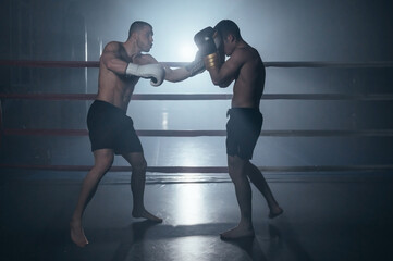 Obraz premium Two shirtless muscular man fighting Kick boxing combat in boxing ring. High quality photo