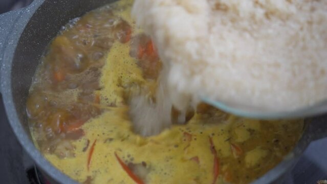 Cook pours rice into a pot with boiling zirvak for pilaf, selective focus