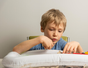 a boy with blond hair plays with sand in an inflatable sandbox for the house.