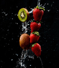 Row of strawberries and kiwi being doused with plenty of water against a black background