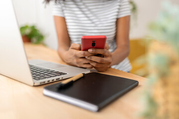 Close-up view of a woman using her mobile phone while working at home. Technology concept.