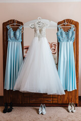Dress and shoes for the bride and her bridesmaids hanging on hangers waiting in wedding ceremony.