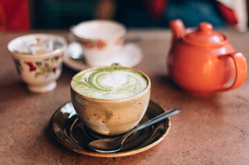 Green Matcha Latte, popular trendy tea with latte art heart shape on top. Served in cafe in ceramic mug on rustic table. Strong shadows and summer sun light