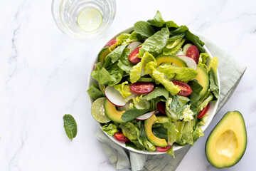 Fresh mix salad leaf with avocado, tomato, cucumber, radish, olive oil on marble table, top view.