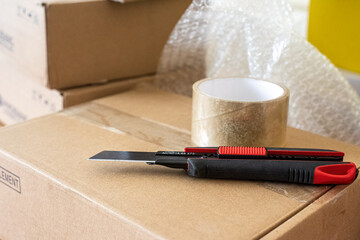 construction knife and sticky transparent tape on the packing box on the desk in the dispatch office