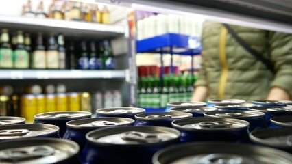Close-up of many blue cans of beer on a store shelf and a man with shopping trolley takes one