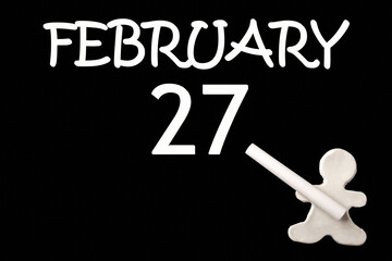 A small white plasticine man writing the date 27 February on a black board. Business concept. Education concept.
