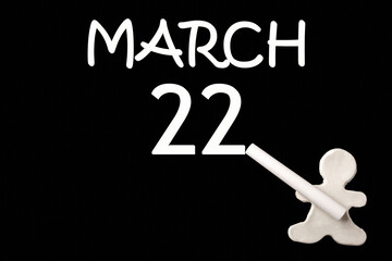 A small white plasticine man writing the date 22 March on a black board. Business concept. Education concept.