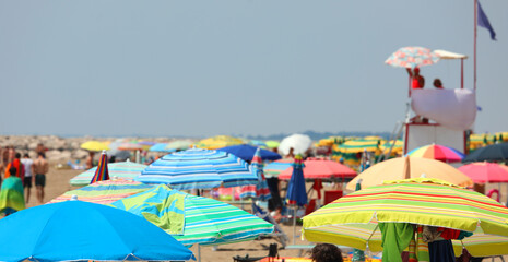 colorful umbrellas on the crowded beach on the sea coast in summer and the lifeguard watchtower