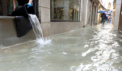 emptying the water from the shop using a bucket during a terrible flood in the island of venice - obrazy, fototapety, plakaty