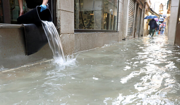emptying the water from the shop using a bucket during a terrible flood in the island of venice
