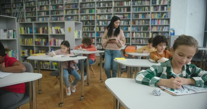 Asian teacher walks between kids watching learning process
