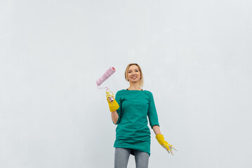 A young girl is engaged in repairs and smiles with a pink roller in her hands against a white wall in a new apartment. Renovation of the interior and a new apartment. 