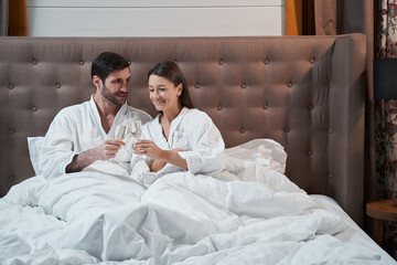 Fototapeta premium Couple clinking their glasses in bed of hotel